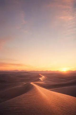 Sunrise over a winding path through desert dunes