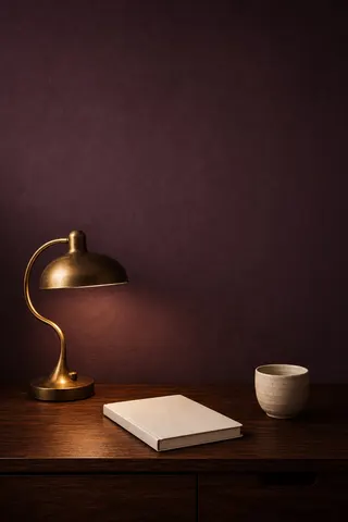 A tidy desk with a brass lamp, a notebook and a cup