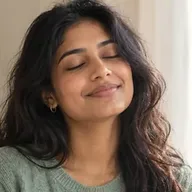 A young woman with her eyes closed, smiling softly in window light